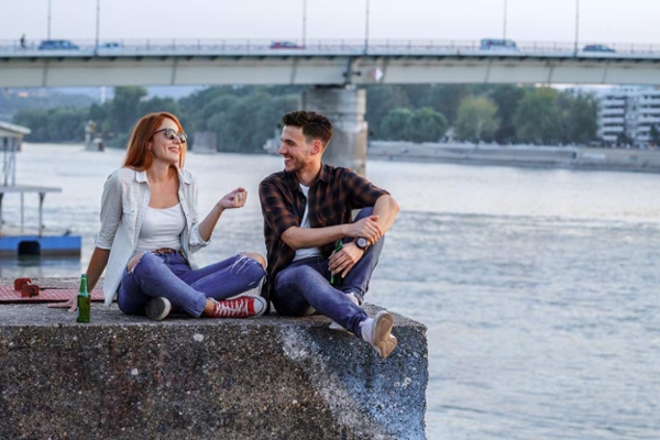 Eine junge Frau und ein junger Mann genießen den Abend auf einer Kaimauer am Fluss. Sie reden – über das Leben, die Zukunft, vielleicht auch über ihre Altersvorsorge. Eine junge Frau und ein junger Mann genießen den Abend auf einer Kaimauer am Fluss. Sie reden – über das Leben, die Zukunft, vielleicht auch über ihre Altersvorsorge.