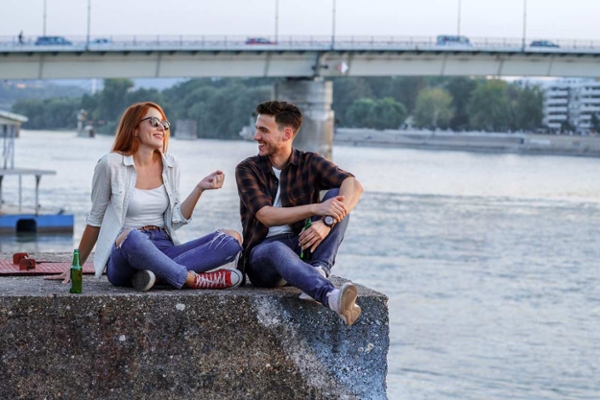 Eine junge Frau und ein junger Mann genießen den Abend auf einer Kaimauer am Fluss. Sie reden – über das Leben, die Zukunft, vielleicht auch über ihre Altersvorsorge.